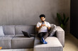 Cool Gadget And Application. Portrait of young smiling Arab man holding mobile phone, typing sms message, sitting on the couch in living room.