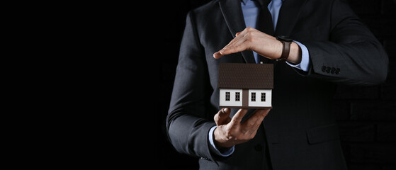 Sticker - Insurance agent with model of house on dark background with space for text