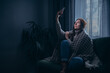 © MZaitsev - A young woman is trying to catch a connection during a power outage. The female sits on a couch in a dark room with no electricity, no communication, and no heating.