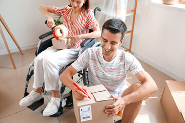 Wall Mural - Young man and his wife in wheelchair packing things in room on moving day