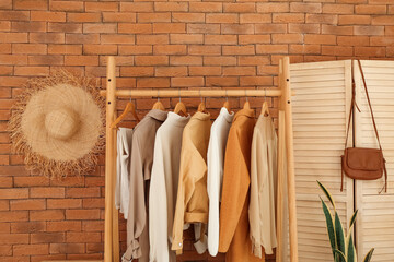 Wall Mural - Rack with stylish clothes and folding screen near brick wall
