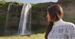 Portrait of woman on Iceland in Icelandic sweater by waterfall outdoor. Candid beautiful female model in nature landscape with tourist attraction Seljalandsfoss waterfall