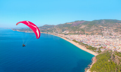 Paraglider flies in the sky, Famous Cleopatra Beach in the background - Alanya, Turkey