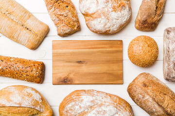 Minimalist wooden cutting board blank mockup on background of Types of homemade bread. Different kinds of fresh bread as background, top view with space for your text or design