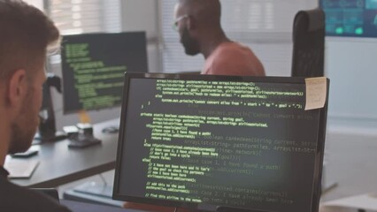Diverse team of professional programmers typing program codes appearing on black screen of their computer monitors, working together in modern office