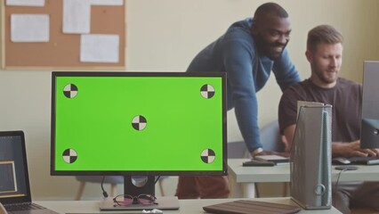 Two multiethnic young programmers discussing new software program while working together in IT office with blank copy space computer monitor on desk in foreground