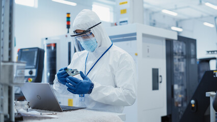 Leinwandbilder - Electronic Manufacturing Factory: Engineer in Sterile Coverall Working on Laptop Computer, Examining a Circuit Board with Microchips and Testing New Electrical Equipment.