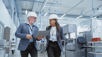 Poster - Portrait of a Two Diverse Heavy Industry Engineers in Hard Hats Walking with Laptop Computer and Talking in a Factory. Footage of Two Manufacturing Employees at Work.