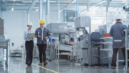 Poster - Portrait of Two Young Asian Heavy Industry Engineers in Hard Hats with Laptop Computer Talking in a Factory. Footage of Two Manufacturing Employees at Work in Production Facility.