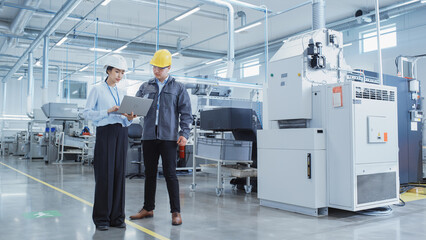 Aufkleber - Two Professional Heavy Industry Employees Wearing Hard Hats at Factory. Walking and Discussing Industrial Machine Facility, Using Laptop Computer. Asian Engineer and Technician at Work.