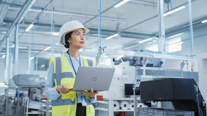 Poster - Portrait of a Happy Asian Female Engineer in Hard Hat Standing and Using Laptop Computer at Electronic Manufacturing Factory. Technician Thinking About Daily Tasks and Working on Development Pipeline.