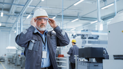 Poster - Close Up Portrait of a Middle Aged, Successful Male Engineer in White Hard Hat and Safety Glasses, Standing at Electronics Manufacturing Factory. Heavy Industry Professional Posing for Camera.