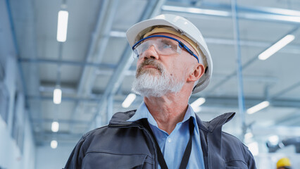 Leinwandbilder - Portrait of a Middle Aged, Successful Male Engineer in White Hard Hat and Safety Glasses, Standing at Electronics Manufacturing Factory. Heavy Industry Specialist Posing for Camera. Low Angle Shot.