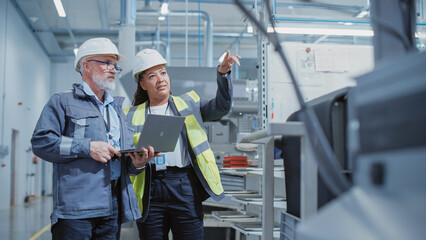 Poster - Portrait of Two Heavy Industry Employees in Hard Hats at Factory. Checking and Discussing Industrial Facility, Using Laptop Computer. African American Engineer and Middle Aged Technician at Work.