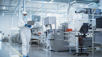 Poster - Heavy Industry Manufacturing Factory: Scientist in Sterile Coverall Walking with Laptop Computer, Examining Industrial CNC Machine Settings and Configuring Production Functionality.