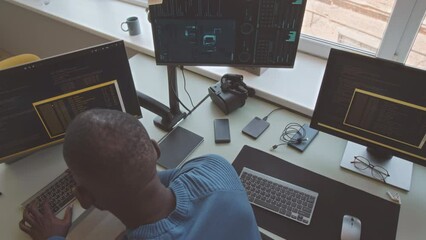 Top view of African American software engineer using laptop, desktop computer, smartphone and other devices while working at office desk