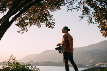 A young Caucasian man with a professional camera in his hands on a mountain by the sea.