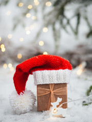 Canvas Print - Gift box in Santa hat on the Christmas tree outdoors, snowy weather. Garland of bokeh