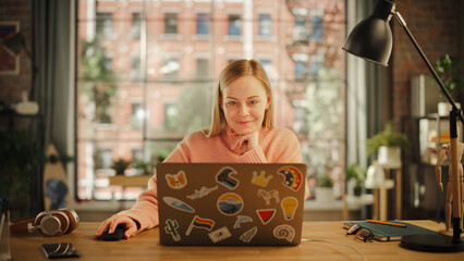 Poster - Beautiful Young Adult Woman Using Laptop Computer with LGBT Stickers on the Back in Creative Loft Office Space. Happy Specialist in Warm Cozy Sweater Working from Home.