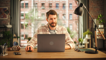Poster - Creative Bearded Man Working on Laptop Computer while Sitting at a Table in Stylish Cozy Loft Living Room. Freelancer Working Remotely. Browsing Internet, Using Social Networks, Thinking on Projects.