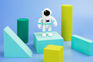 Wall Mural - Plastic figurine of an astronaut in a spacesuit and geometric shapes on a blue background. Children's toy astronaut. Fascination with space, the study of planets.