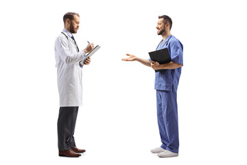 Wall Mural - Full length profile shot of a male doctor standing and writing a document and talking to a healthcare worker
