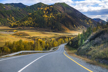 Serpentine Asphalt Road Among High Snow-capped Mountain Peaks, Yellow Desert, Autumn Green Forest And Blue Sky. Car On The Highway Against The Background Of A Mount Landscape.