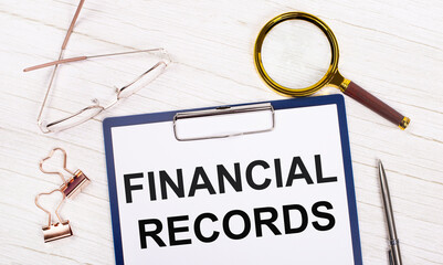 Fototapete - A tablet with the text FINANCIAL RECORDS on white paper, a magnifier, glasses, golden paper clips and a pen lie on a white office table. Top view, flat lay.