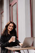 © Rabizo Anatolii - Cheerful young woman is working online on laptop and sitting on summer terrace in cafe. Happy excited girl with cup of coffee and laptop is enjoying her lifestyle outside of cafe.