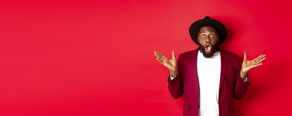 Fashion and party concept. Impressed Black man in classy outfit staring with complete disbelief at camera, gasping and looking surprised, standing over red background