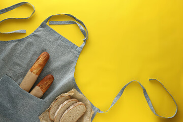 Poster - Clean kitchen apron with different types of bread on yellow background, flat lay. Space for text