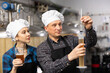Man and woman brewmasters measuring portion of beer with alcoholometer.