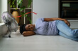 © DimaBerlin - Overheated African woman lying on floor sleeping with electric fan on, enjoying fresh air, exhausted black female resting at home during extremely hot weather. Staying cool without air conditioning