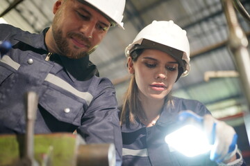 Young successful technician or repairman of industrial machines in safety helmet and workwear standing in large garage or workshop