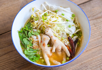 Wall Mural - Rice noodles with chicken feet on soup bowl on wooden table food background - Thai food thai rice noodles spicy soup curry with fresh vegetable