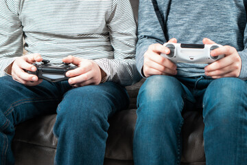 Male hands hold modified plastic joysticks. Friends play videogames sitting on couch. Two people hold wireless game console. Press buttons on controller by fingers. Modern technologies and gaming.