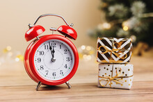 Red Alarm Clock And White Gift Boxes Tied Golden Ribbons And Bow On Wooden Background. Merry Christmas And Happy New Year Holiday Greeting Card. Copy Space