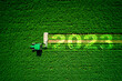 Leinwandbild Motiv 2023 Happy New Year agriculture concept. Red agricultural tractor mowing green field, aerial view