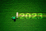 2023 Happy New Year agriculture concept. Red agricultural tractor mowing green field, aerial view