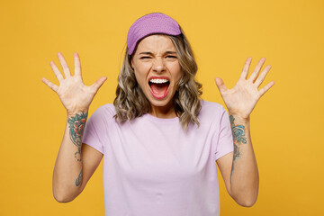 Calm young angry sad furious irritated woman she wearing purple pyjamas jam sleep eye mask at home scream spread hands isolated on plain yellow background studio portrait. Bad mood night nap concept.