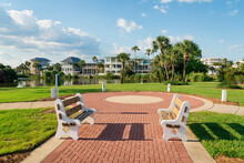 Destin, Florida- Two Benches On A Bricks Pavement In The Middle Of Green Grass Near The Lake
