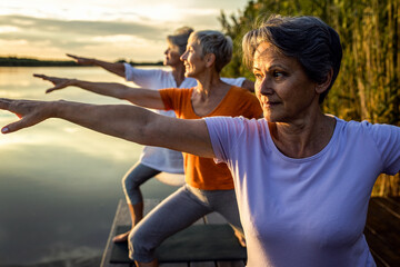 Wall Mural - Group of senior woman doing yoga exercises by the lake.