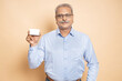 © GAJENDRRA BHATI  - Happy senior Indian man holding blank business or debit credit card in hand isolated on beige background.