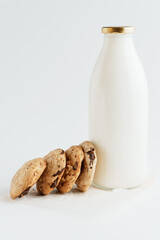 Cookies with pieces of chocolate next to a bottle of milk on a white background