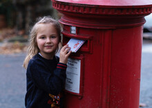 Cute Girl Is Posting A Letter For Santa Claus Into The Classic Red English Postbox. Popular Children Christmas Activity.
