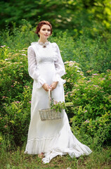 Wall Mural - Beautiful girl in a vintage long white dress, and a hairstyle in the English style in a summer park, with a basket in hand, warm summer