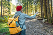 © Shi  - Wanderlust and travel concept. Stylish traveler girl in cap looking at mountains, exploring woods. Young woman traveling with a yellow backpack and in sportswear navigating for direction in the