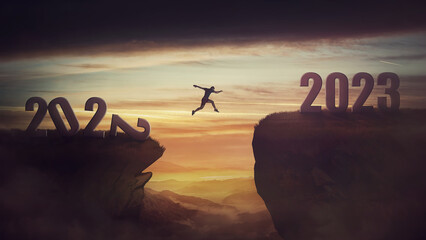 Determined man jump over a chasm obstacle to reach the new 2023 peak and let 2022 behind. Conceptual and surreal sunset scene, new year motivational background. Leader overcoming hurdles reach highs