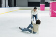Young man in sweater helping to african american girlfriend on ice rink