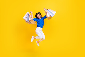 Canvas Print - Full length photo of sweet lucky girl dressed blue shirt jumping high rising shoppers isolated yellow color background